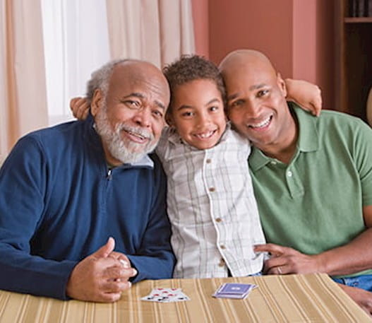 A young boy sitting between his grandfather and father. All three are smiling.