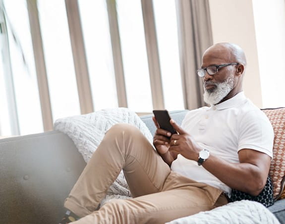 An elderly man sits on his couch looking at his phone