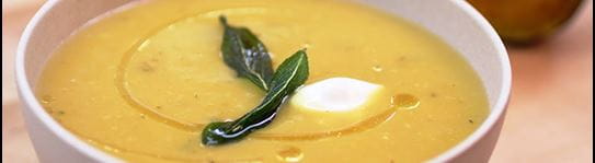 A bowl of butternut squash soup with a bayleaf and spoonful of cream in the centre 