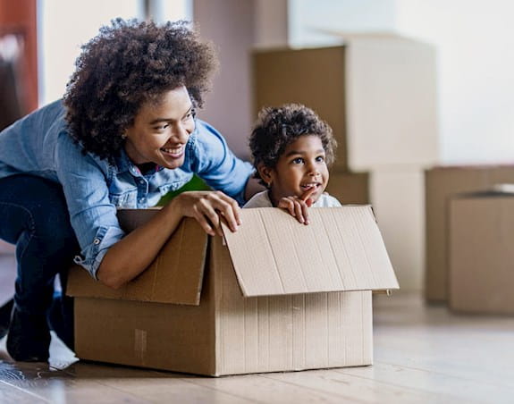 A parent and child playing in a cardboard box on moving day.