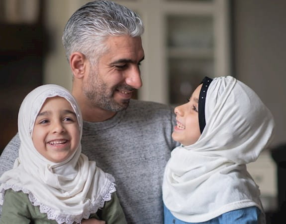 A father with his two young daughters wearing hijabs.