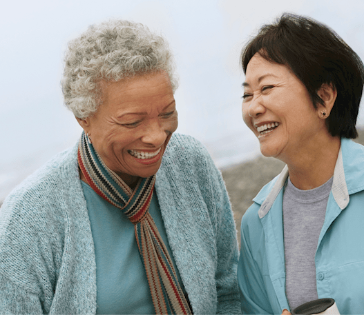 Two elderly women laugh with each other at the beach