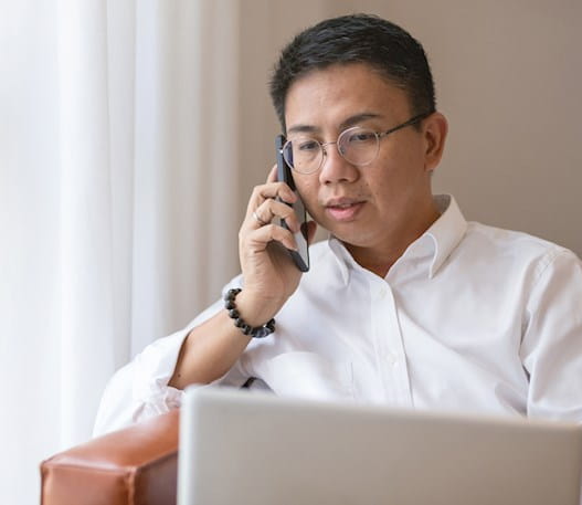Homme regardant l’écran de son ordinateur portable en parlant au téléphone cellulaire.