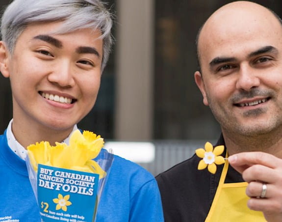 Two volunteers holding daffodils and a daffodil pin