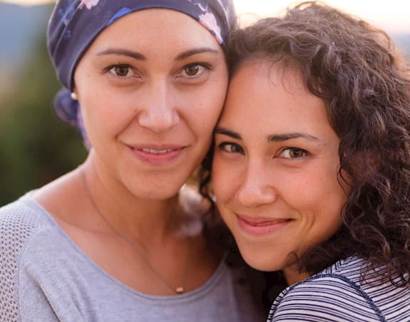 Une femme atteinte de cancer, un foulard sur la tête, qui sourit, en compagnie d’une autre femme.