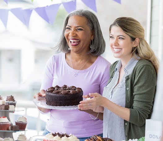 Une femme âgée et une jeune femme tenant un gâteau au chocolat et souriant à une autre femme.