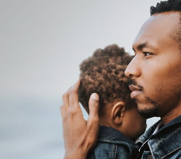 Un homme regardant au loin en tenant la tête de son jeune fils près de lui. 