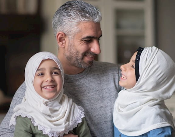 Un père avec ses deux jeunes filles portant des hijabs.