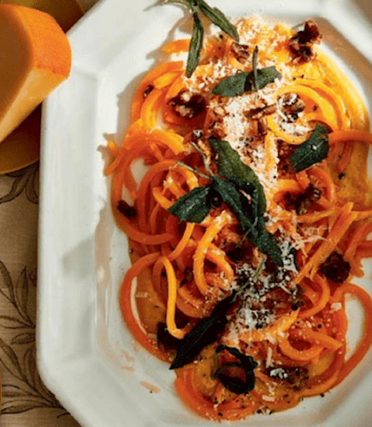A plate of butternut squash topped with fried sage anda grated gouda cheese.